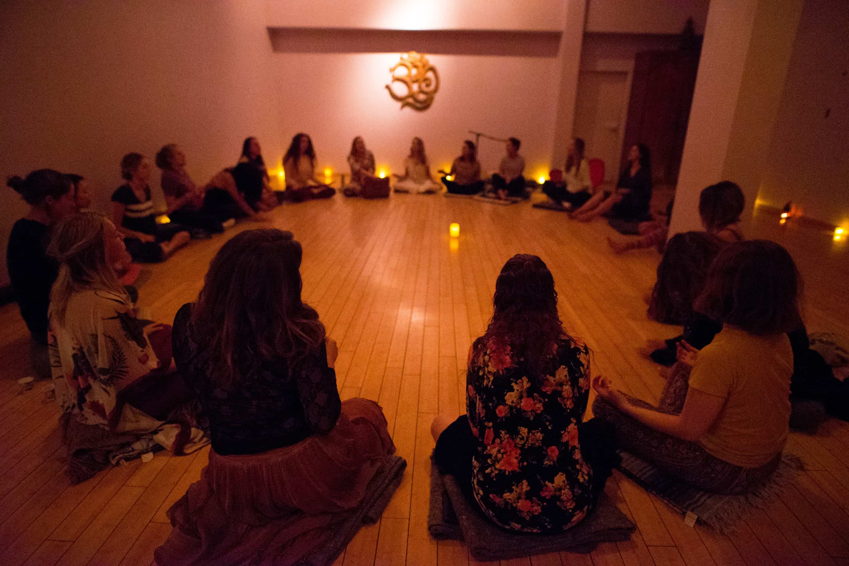 A group of women in a yoga meditation room sitting in a class with lights dim.